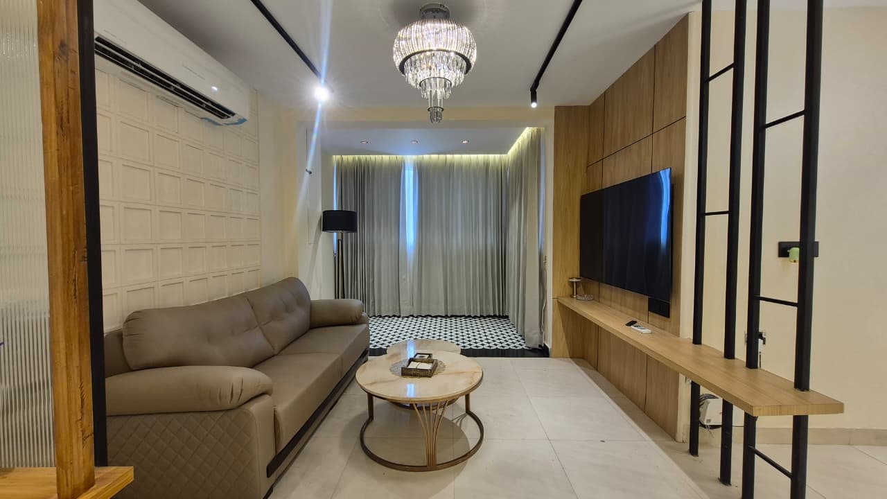 Elegant living room with veneer paneled TV wall, leather sofa, and crystal chandelier